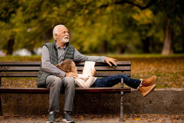 秋の日に孫と一緒に公園のベンチで過ごすハンサムな祖父 — ストック写真