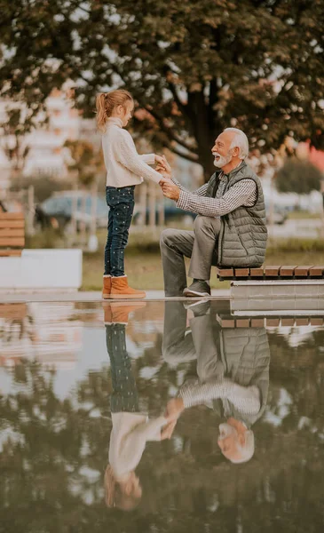 秋の日に孫と一緒に公園の小さなプールで過ごすハンサムな祖父 — ストック写真