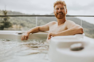 Attractive young man enjoying in outdoor hot tub on vacation