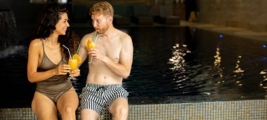 Yakışıklı genç çift havuz kenarında rahatlıyor ve portakal suyu içiyor.