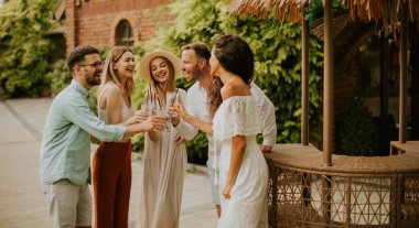 Bir grup mutlu genç dışarıda içkiyle eğleniyor ve tezahürat yapıyor.