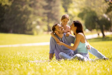 Küçük tatlı kızıyla mutlu bir aile güneşli bir günde parkta eğleniyor.