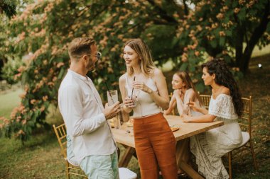 Group of young people cheering with fresh lemonade and eating fruits in the garden