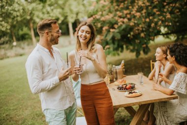 Group of young people cheering with fresh lemonade and eating fruits in the garden