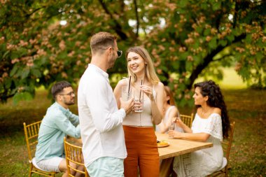 Group of young people cheering with fresh lemonade and eating fruits in the garden