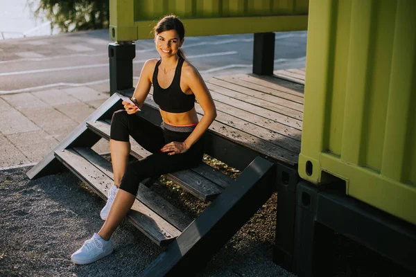 观看年轻女子在室外锻炼和使用手机时休息的情景 — 图库照片