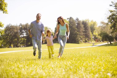 Küçük tatlı kızıyla mutlu bir aile güneşli bir günde parkta eğleniyor.