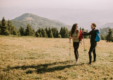 Smiling young couple preparing hiking adventure with backpacks by terrain vehicle