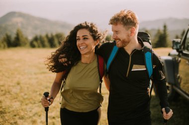 Sırt çantaları yeşil tepelerde yürüyen gülümseyen genç çift.