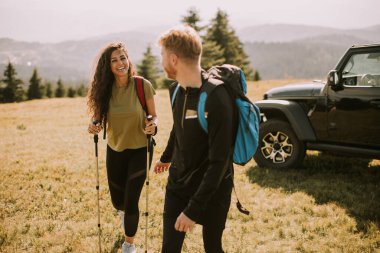 Sırt çantaları yeşil tepelerde yürüyen gülümseyen genç çift.
