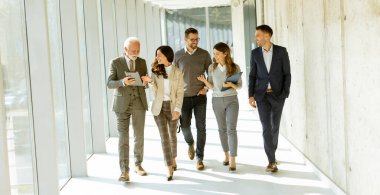 Bir grup şirket çalışanı güneşli bir günde ofis koridorunda yürüyorlar.
