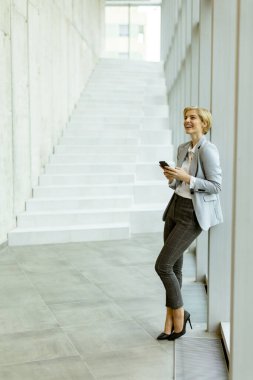 Modern ofis koridorunda dururken cep telefonu kullanan iş kadını.