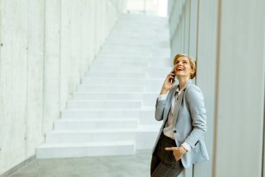 Modern ofis koridorunda dururken cep telefonu kullanan iş kadını.