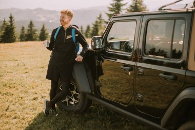 Handsome young man relaxing on a terrain vehicle hood at countryside