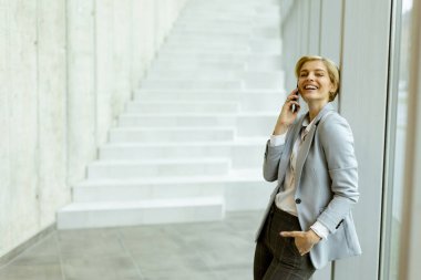 Modern ofis koridorunda dururken cep telefonu kullanan iş kadını.