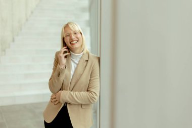 Modern ofis koridorunda dururken cep telefonu kullanan iş kadını.