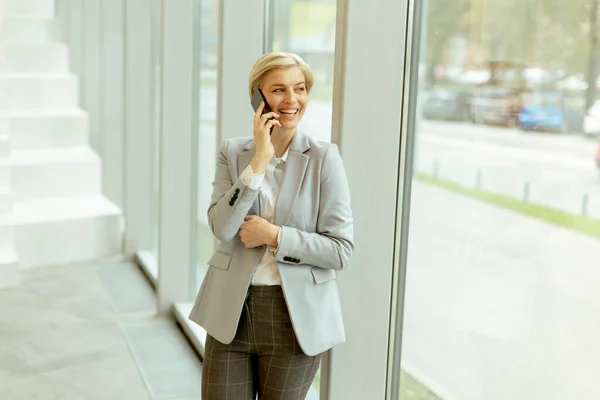 Pengusaha Wanita Menggunakan Ponsel Saat Berdiri Lorong Kantor Modern — Stok Foto