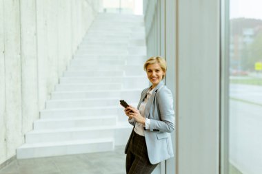 Modern ofis koridorunda dururken cep telefonu kullanan iş kadını.