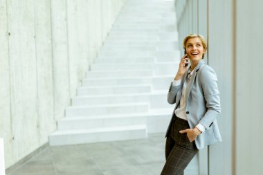 Modern ofis koridorunda dururken cep telefonu kullanan iş kadını.