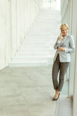 Modern ofis koridorunda dururken cep telefonu kullanan iş kadını.