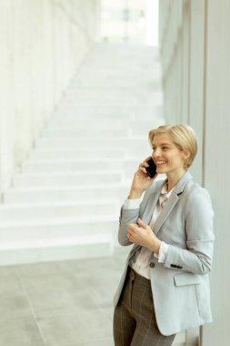 Modern ofis koridorunda dururken cep telefonu kullanan iş kadını.