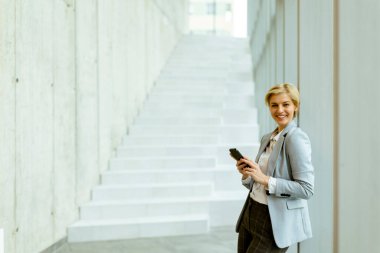 Modern ofis koridorunda dururken cep telefonu kullanan iş kadını.