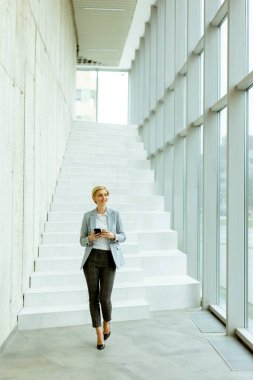 Modern ofis koridorunda yürürken cep telefonu kullanan iş kadını