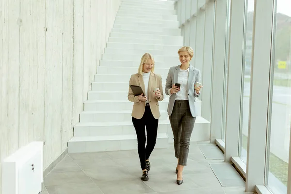 Två Affärskvinnor Går Med Digital Surfplatta Och Mobiltelefon Kontorskorridoren — Stockfoto