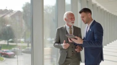 Yakışıklı iş adamı ve genç meslektaşı ofis koridorunda dijital tablet hakkında finansal rapor tartışıyorlar.