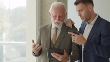 Yakışıklı iş adamı ve genç meslektaşı ofis koridorunda dijital tablet hakkında finansal rapor tartışıyorlar.