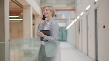 Modern ofis koridorunda cep telefonu kullanan bir iş kadını.