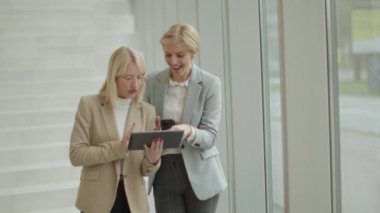 Ofis koridorunda dizüstü bilgisayarı ve cep telefonu olan iki iş kadını.