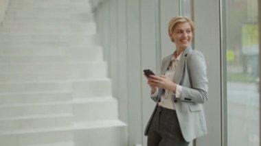 Modern ofis koridorunda cep telefonu kullanan bir iş kadını.