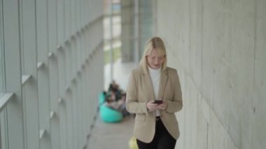 Modern ofis koridorunda cep telefonu kullanan bir iş kadını.