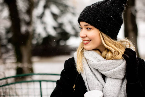 可愛いです若い女性暖かい服で楽しむ雪の中でテイクアウトコーヒーカップ — ストック写真
