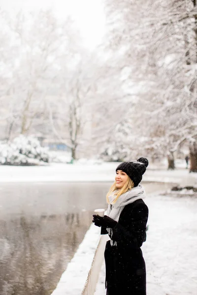 漂亮的年轻女子穿着保暖的衣服 拿着外卖的咖啡杯在雪地里享受着 — 图库照片