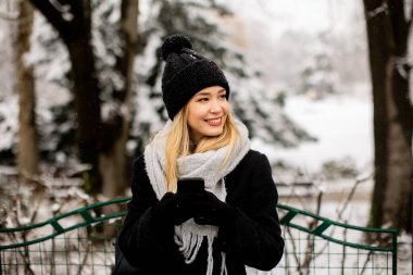 Pretty young woman in warm clothes using mobile phone on a winter day