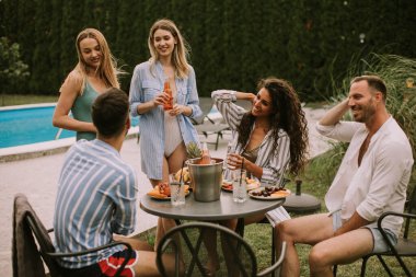 A group of young adults enjoying a leisurely summer party with food, drinks in the backyard