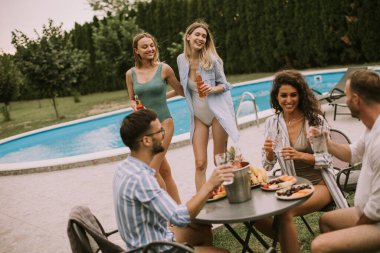 Group of happy young people cheering with cider by the pool in the garden