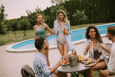 Group of happy young people cheering with cider by the pool in the garden