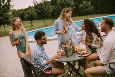 Group of happy young people cheering with cider by the pool in the garden