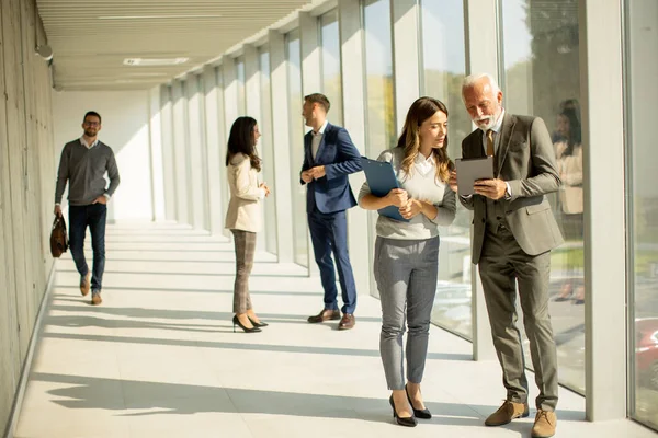 stock image Handsome senior business man with his young female coleague using digital tablet in the office corridor