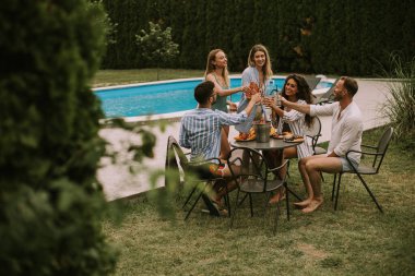 Group of happy young people cheering with cider by the pool in the garden
