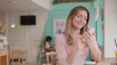 Laptop üzerinde çalışırken cep telefonu kullanan ve kafede taze portakal suyu içen güzel bir kadın.