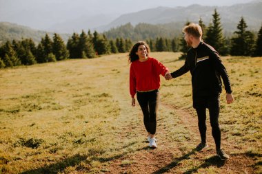 Smiling young couple walking over green hills