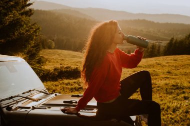 Pretty young woman relaxing on a terrain vehicle hood at countryside