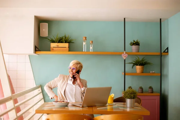 Mulher Sênior Usando Telefone Celular Enquanto Trabalhava Laptop Tomando Café — Fotografia de Stock