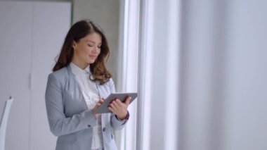 Ofis koridorunda dijital tablet üzerinde çalışan güzel genç bir kadın.