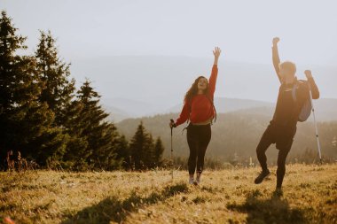 Sırt çantaları yeşil tepelerde yürüyen gülümseyen genç çift.