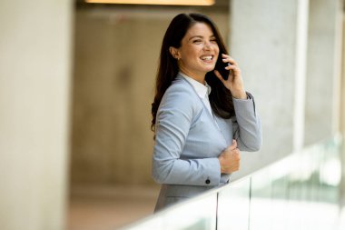 Ofis koridorunda cep telefonu kullanan genç ve güzel bir iş kadını.